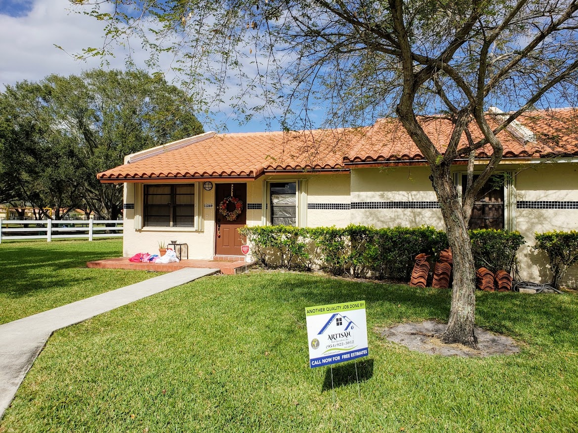 Completed terracotta tile roof replacement on single-story South Florida home with Artisan yard sign
