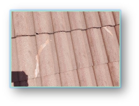 Cracked concrete barrel tiles with visible fracture lines running across the tile field – clay tile damage requiring repair