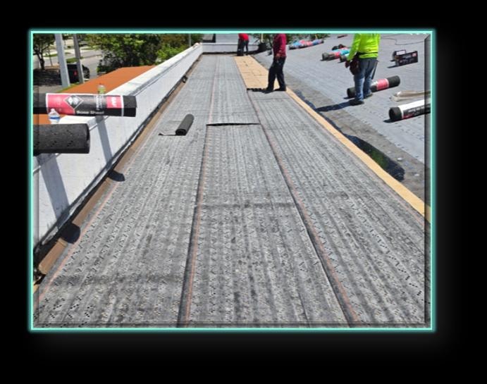 Flat roof base sheet installation in progress – workers rolling out modified bitumen base sheet across commercial flat roof deck
